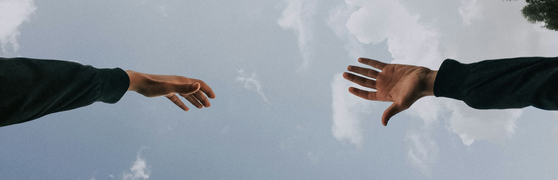 Hands reaching toward each other with sky in background